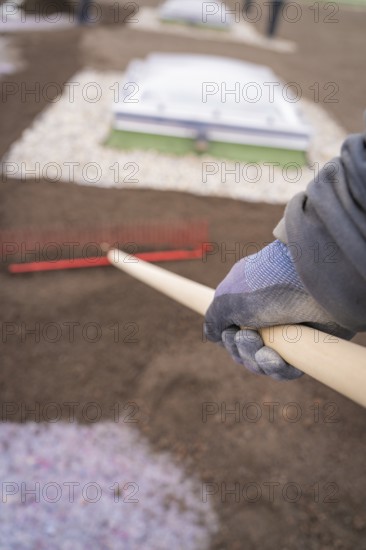 Close-up of a worker working the soil on a roof with a rake, roof greening, house construction, climate neutral