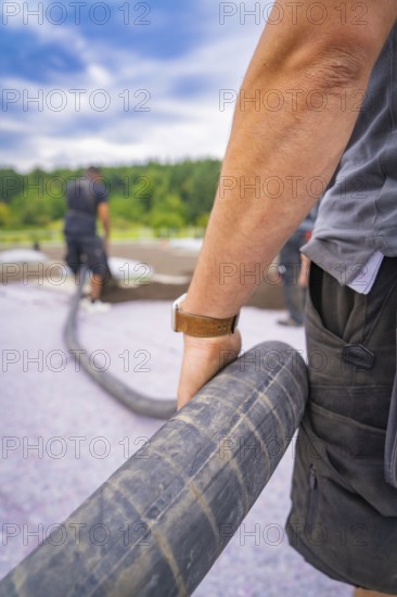 Close-up of a worker holding a thick hose during construction work, roof greening, house construction, climate neutral