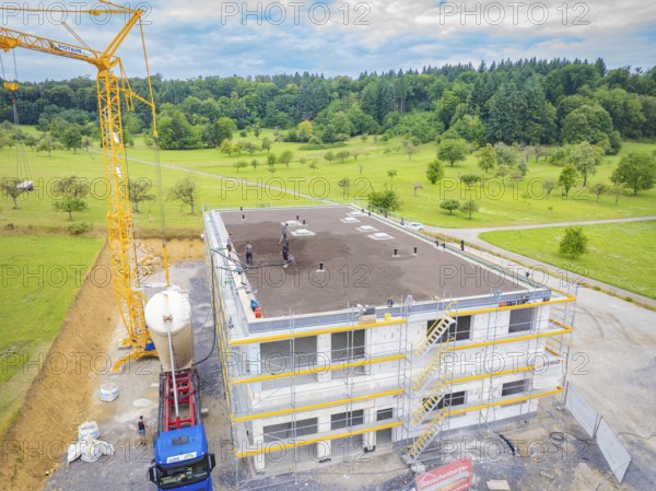 Large building shell with crane and workers in a rural setting, green roof, house construction, climate neutral