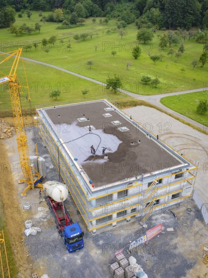 Building shell with crane and workers on a construction site surrounded by green areas, green roof, house construction, climate neutral
