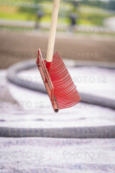 A free-floating red rake in front of a roof with a blurred background in a construction site environment, roof greening, house construction, climate neutral