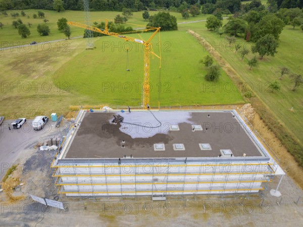 Drone shot of a construction site with crane and partially constructed building on a large green area, green roof, house construction, climate neutral