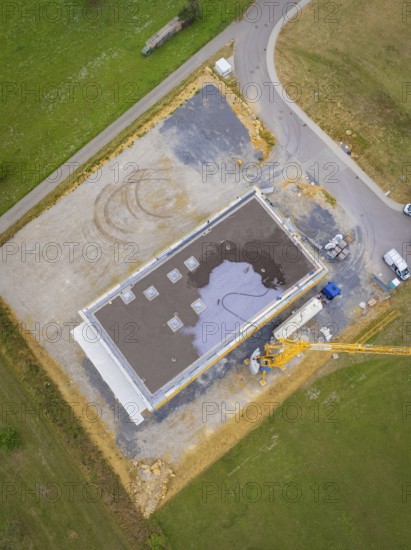 Aerial view of a rectangular building in shell construction on a large site next to a road, green roof, house construction, climate neutral
