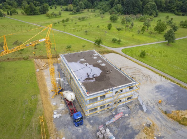 Drone view of a construction site with construction workers, crane and vehicles on a green area, green roof, house construction, climate neutral