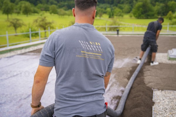 A worker in construction clothing holds a hose, with a view of a green landscape, roof greening, house construction, climate neutral