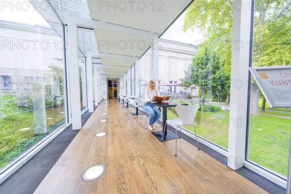 Woman sitting in a bright café with glass walls and a green garden view, Frieder Burda Museum, Baden Baden, Germany