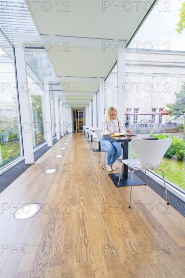 Woman sitting at a table in a light-flooded café with large glass walls, Frieder Burda Museum, Baden Baden, Germany