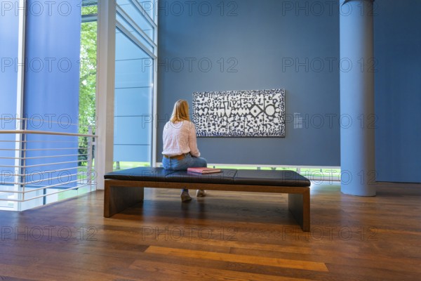 A woman sits on a bench in front of a modern work of art and looks at it attentively, Frieder Burda Museum, Baden Baden, Germany