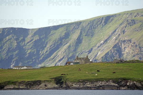 A remote house stands in green pasture against a dramatic mountain backdrop, Sumburgh, Shetland Islands, Scotland, United Kingdom