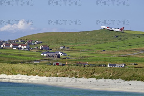 An aeroplane takes off over wide meadows and a coastal village with sea views, Sumburgh Head, Shetland Islands, Scotland, United Kingdom