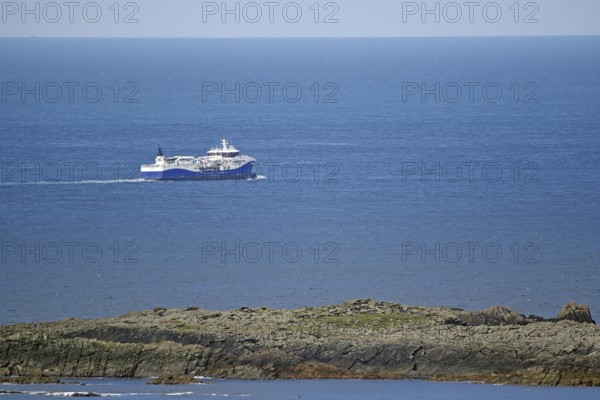 A large fishing vessel navigates the blue sea along the rocky coastline, Sumburgh Head, Shetland Islands, Scotland, United Kingdom
