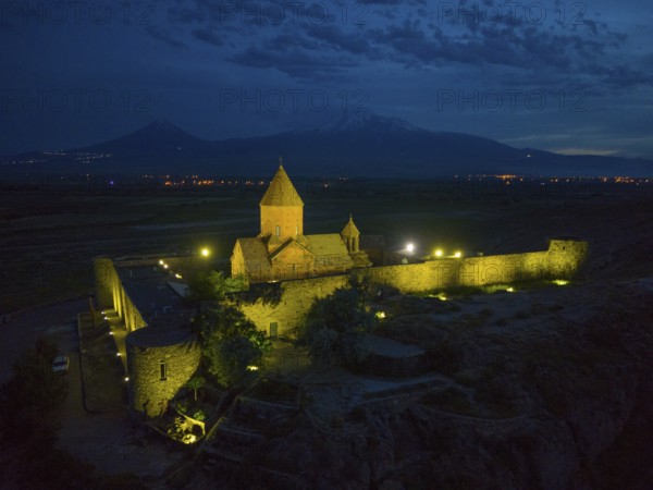 Illuminated monastery at night with mountains and shining stone walls, aerial view, Chor Wirap monastery, deep dungeon, in the background the Ararat and the small Ararat, located in Turkey, Ararat province, Armenia