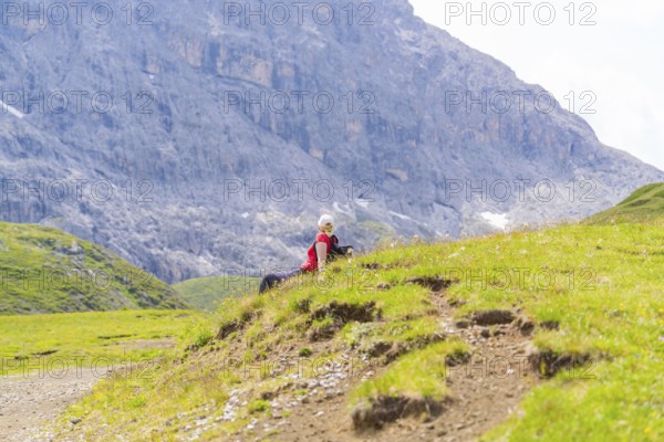Person sitting on a green meadow with rocky mountains in the background, Alpe di Siusi, Dolomites, South Tyrol, Italy