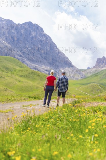 Couple hiking on a mountain path, surrounded by green meadows and mountains, Alpe di Siusi, Dolomites, South Tyrol, Italy