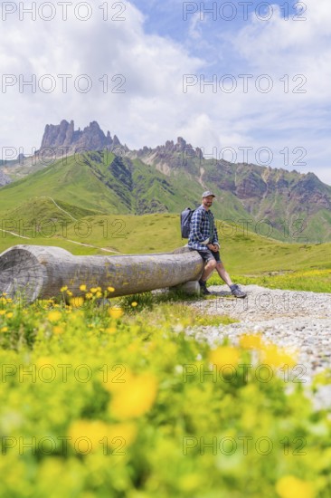 Man in the mountains sitting on a wooden bench, surrounded by green meadows and flowers, Alpe di Siusi, Dolomites, South Tyrol, Italy