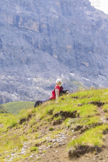 Person sitting on a green meadow, surrounded by rocky mountains under a blue sky, Alpe di Siusi, Dolomites, South Tyrol, Italy