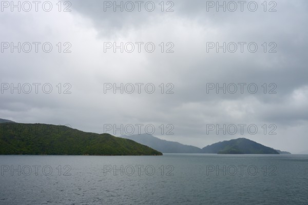 View of calm sea with cloudy sky and green islands, summer, Cook Strait, North Island, South Island, New Zealand