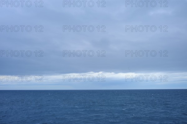 A calm sea stretches to the horizon with thick clouds in the sky, summer, Cook Strait, North Island, South Island, New Zealand
