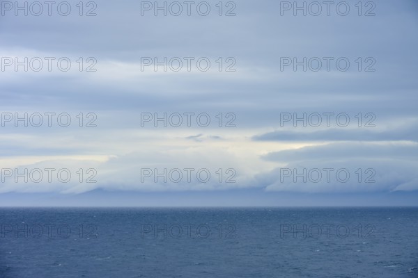 Calm sea under a dense canopy of clouds, mountains visible in the distance, summer, Cook Strait, North Island, South Island, New Zealand