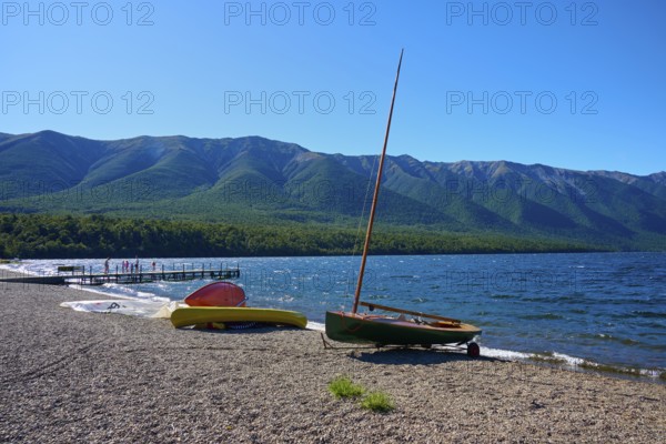 Boats moored on the shore of a lake with a breathtaking mountain backdrop and clear blue sky, summer, Lake Rotoiti, Saint Arnaud, Tasman Region, South Island, New Zealand