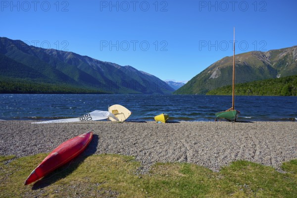 Stored kayaks lying on a beach with a lake and mountains in the background under a clear sky, summer, Lake Rotoiti, Saint Arnaud, Tasman Region, South Island, New Zealand