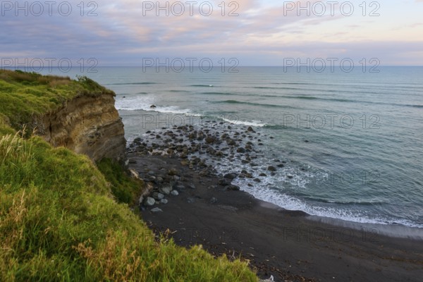 Seaside cliff with rocks and green vegetation under a cloudy sky, summer, Opunake, Taranaki, North Island, New Zealand