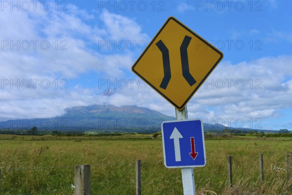 Road signs in front of a volcanic landscape Mount Taranaki under blue sky with clouds, summer, Opunake, Taranaki, North Island, New Zealand