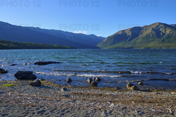 Waves crashing on a pebbly shore, surrounded by impressive mountains and clear blue skies, summer, Lake Rotoiti, Saint Arnaud, Tasman Region, South Island, New Zealand