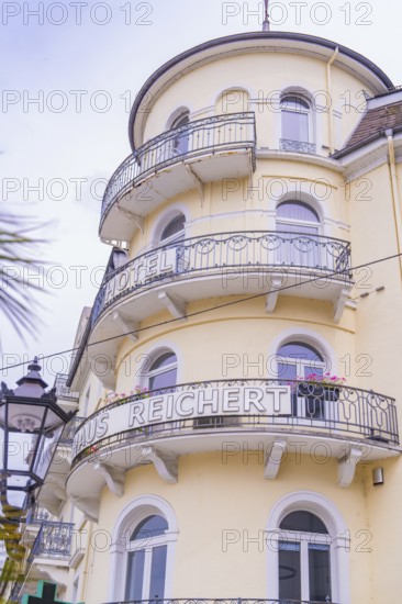 Historic hotel building in yellow with round balconies and surrounding lantern under a cloudy sky, Baden Baden, Germany