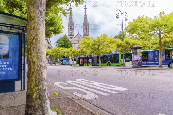 View of a street with trees and buses, a church with two towers rises in the background, Baden Baden, Germany