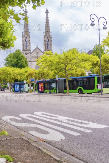 An urban street with buses, flanked by trees, gothic church towers visible in the background, Baden Baden, Germany