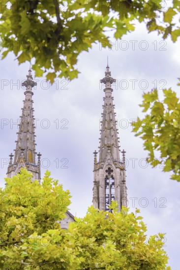 Two gothic church towers visible through the foliage of trees against an overcast sky, Baden Baden, Germany