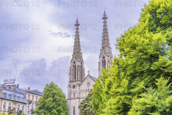 A gothic church with high towers in the background, surrounded by lush green foliage, Baden Baden, Germany
