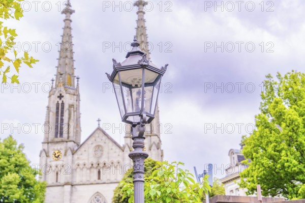 A classic street lamp stands in the foreground, behind it the towers of an impressive Gothic church, Baden Baden, Germany