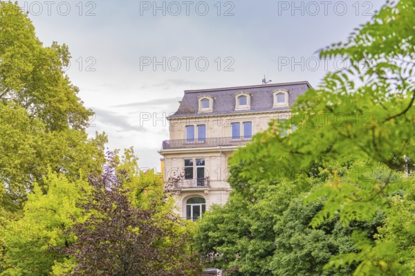Classic building with numerous windows behind dense trees on a cloudy day, Baden Baden, Germany