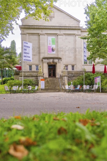 Historic building with signs and stairs, surrounded by trees and outdoor garden furniture, Baden Baden, Germany