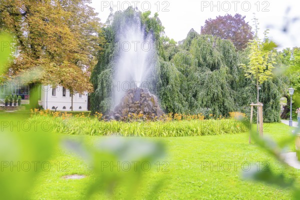 A bubbling fountain in a green park, surrounded by lush trees and flowers, creates a calm and relaxing atmosphere, Baden Baden, Germany