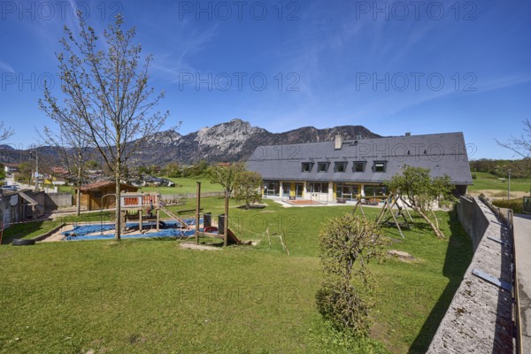 Catholic kindergarten St.Bruder Klaus, building, playground equipment, swing, sandpit, meadow, trees, mountain landscape, mountains, blue sky, cirrostratus clouds, Bayerisch Gmain, district Berchtesgadener Land, Bavaria, Germany