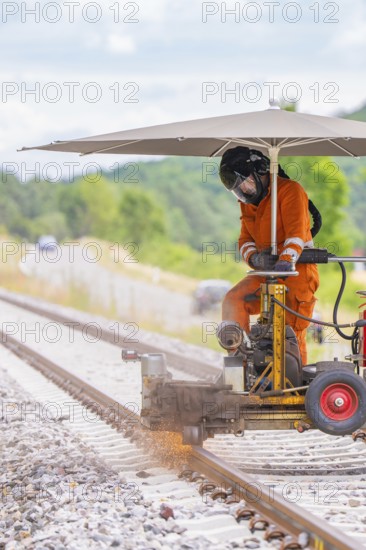 A worker works with machines on a railway track under an umbrella, grinding work on the Hermann Hesse railway, Ostelsheim, district of Calw, Germany