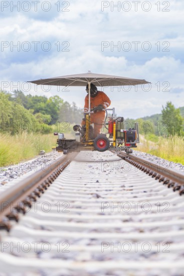 Wide view of a worker in orange on a railway line with an umbrella, grinding work on the Hermann Hesse railway, Ostelsheim, district of Calw, Germany