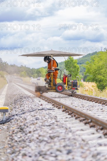 Worker working on the track with a machine under a canopy in a scenic setting, grinding work on the Hermann Hesse railway, Ostelsheim, district of Calw, Germany