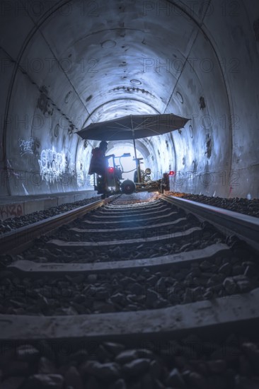 A mysterious tunnel with rails and graffiti, illuminated by a diffuse light. A figure stands under an umbrella, grinding work on the Hermann Hesse railway, Ostelsheim, district of Calw, Germany