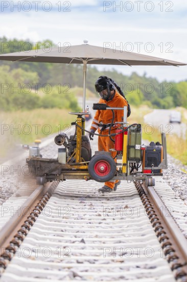 A worker with machines on a railway line, protected by an umbrella, grinding work on the Hermann Hesse railway, Ostelsheim, district of Calw, Germany