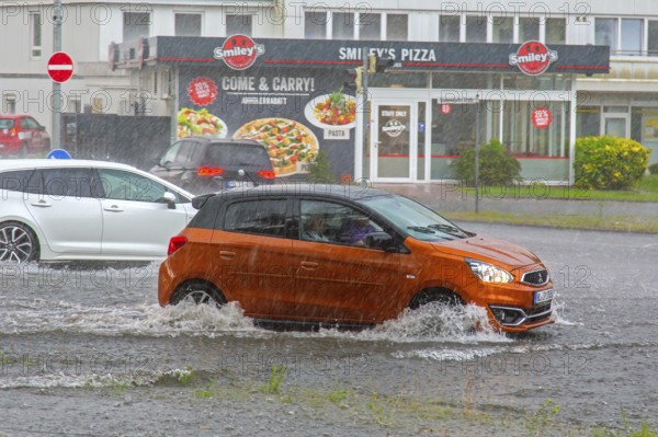 Cars in torrential rain driving through flooded street in town after a heavy downpour, rainfall during thunderstorm in summer, Germany