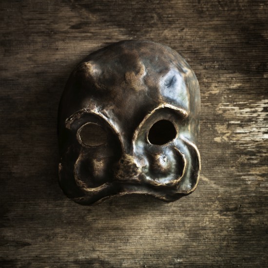 A handcrafted skull mask rests on a weathered wooden surface, highlighting its unique shape and texture. The mask features hollow eye sockets and a distinct design, emphasizing artistry