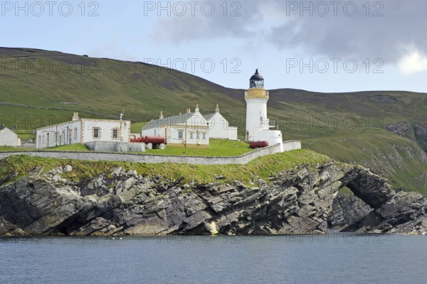 A lighthouse stands on green cliffs with neighbouring buildings, Robert louis Stevenson, boat tour, Noss, Shetland Islands, Scotland, Great Britain