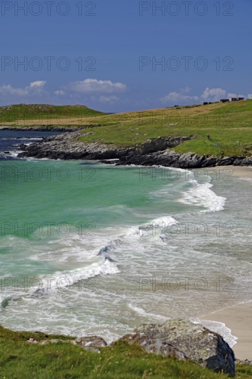 Picturesque coastal landscape with green water and waves meeting the sandy beach under a blue sky, Meal Beach, Scalloway, Shetland Islands, Scotland, United Kingdom