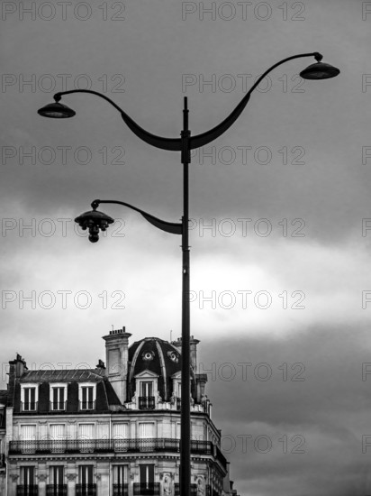 An ornate street lamp rises high against a backdrop of a moody, cloud-filled sky, highlighting the beautiful details of classic architecture that reflects Paris's rich history. France