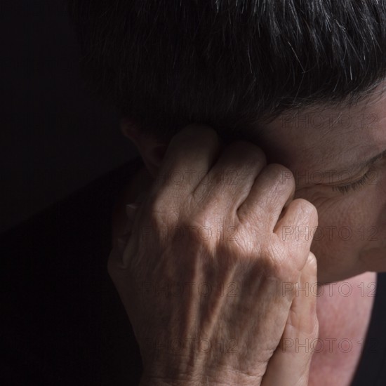 A woman with short hair rests her head on her hand, conveying deep contemplation and introspection in low lighting, creating a somber atmosphere in an intimate setting