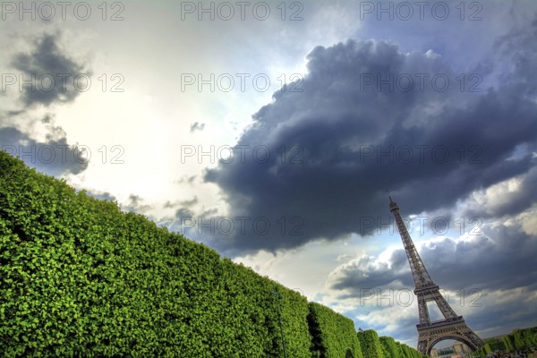 Clouds blanket the sky above the Eiffel Tower, creating a striking contrast with the greenery below. Visitors admire the landmark, capturing its unique allure in this Parisian setting